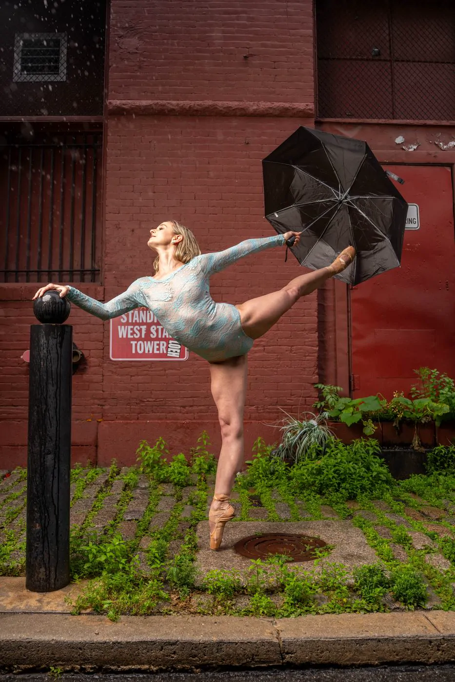Dancer with an umbrella mid-arabesque by a brick wall