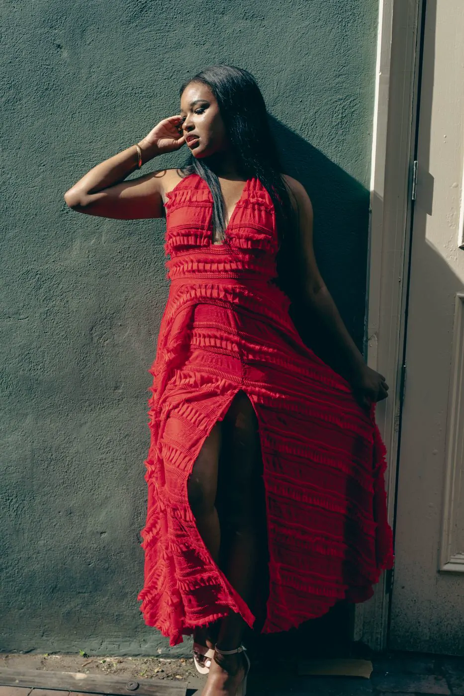 Woman in a flowing red dress posing against a teal wall