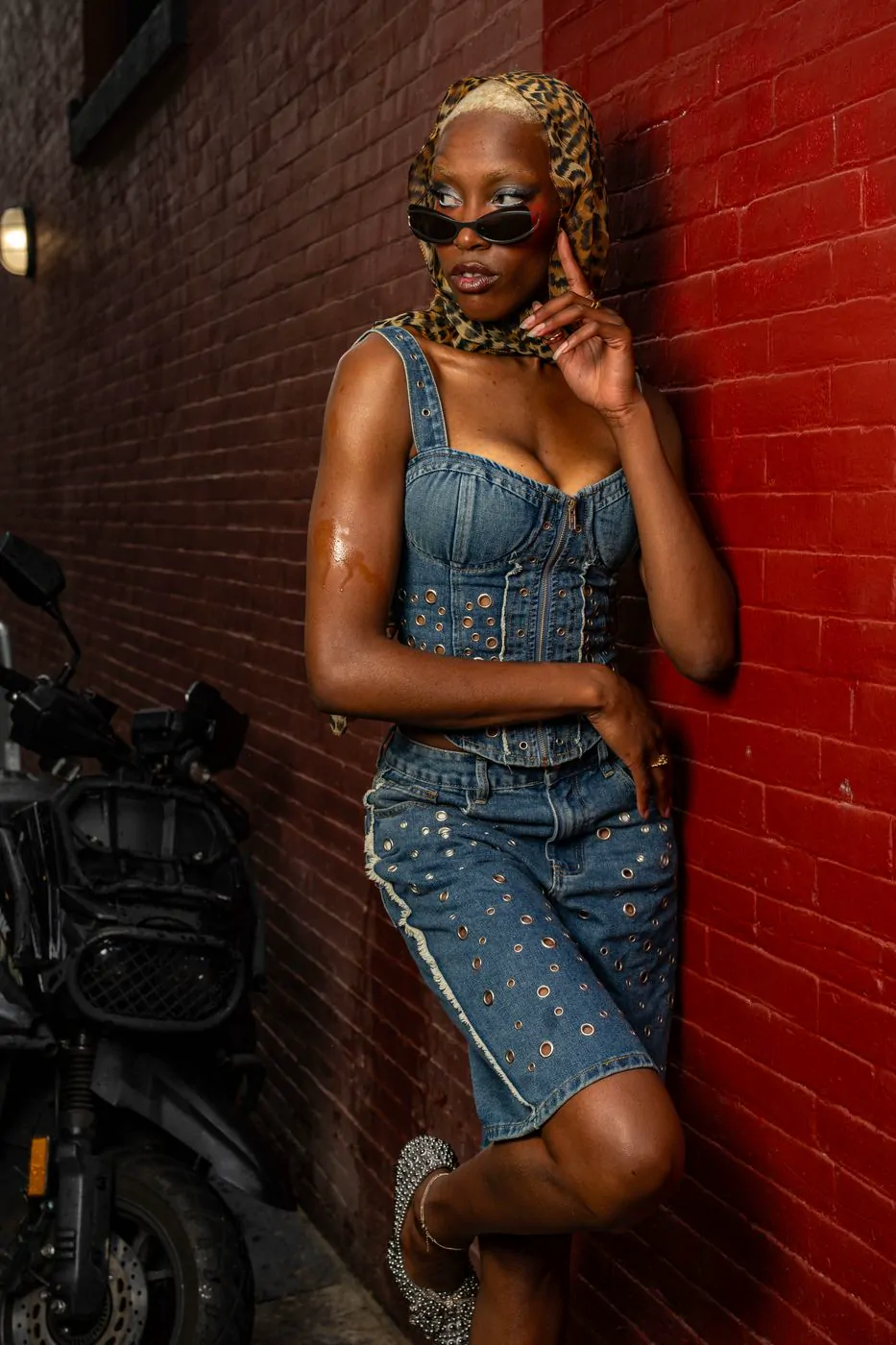Woman in a denim corset and skirt with a leopard scarf against a red brick wall