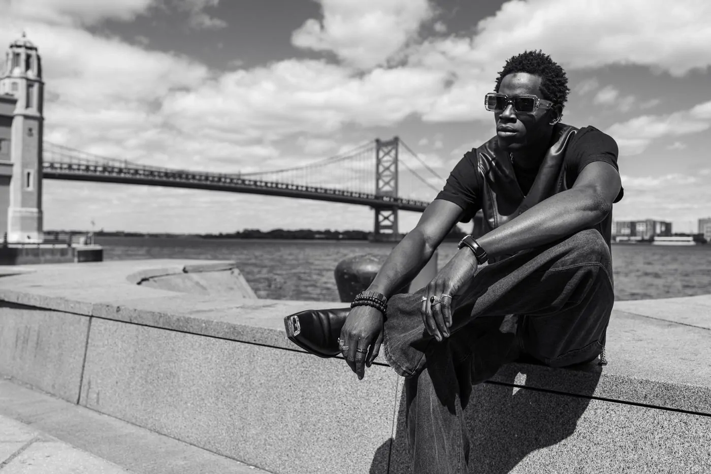 Black and white portrait of a man in sunglasses in front of a suspension bridge