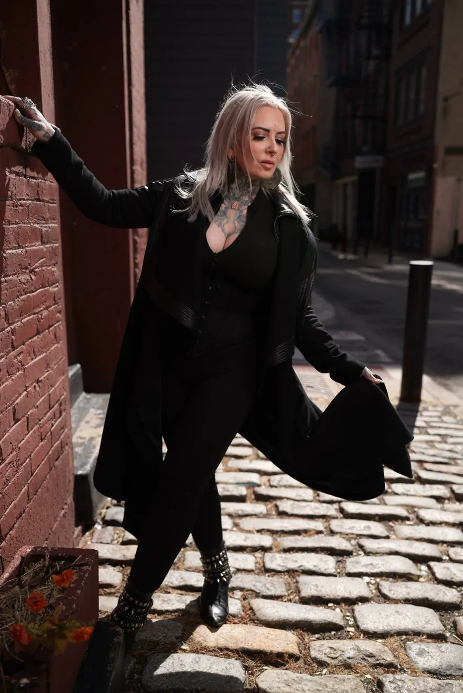 Woman in a long black coat posing on a cobblestone street